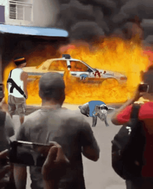 a man with a gun stands in front of a car that is on fire