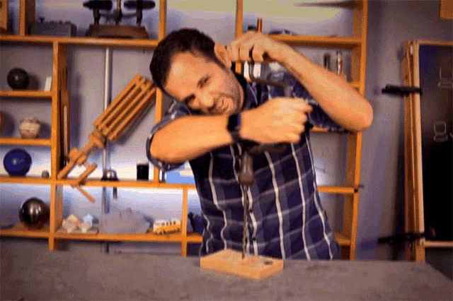a man in a plaid shirt is hammering a nail into a wooden box