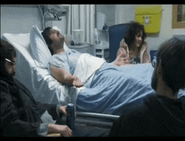 a man is laying in a hospital bed while a woman looks on