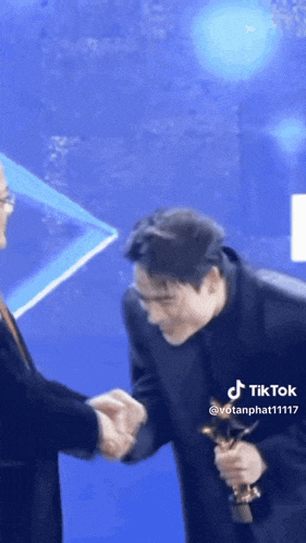 a man in a suit and tie is shaking hands with another man holding a trophy .
