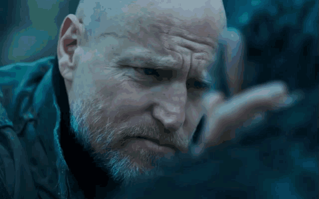 a bald man with a beard looks at something in the dark