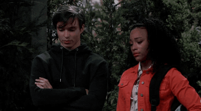 a man in a black hoodie and a woman in a red jacket are standing next to each other