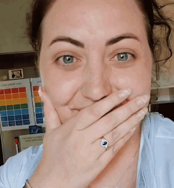 a woman covering her mouth with her hand in front of a fridge with a calendar on it