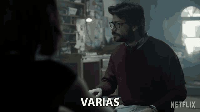 a man in a red sweater talks to a woman in a dark room with the words " varias " above him