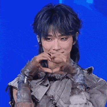 a young man with blue hair is wearing a jacket and gloves and making a face .