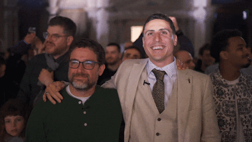 a man in a suit and tie stands next to another man with his arm around his shoulder