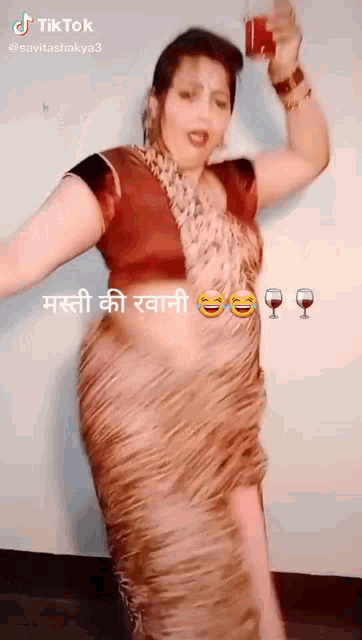 a woman in a saree is dancing and holding a glass of wine in her hand .