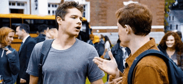two young men are standing next to each other and talking in front of a school bus .