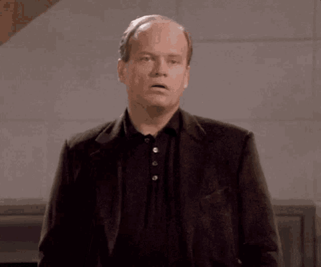a bald man in a suit and black shirt is standing in a room