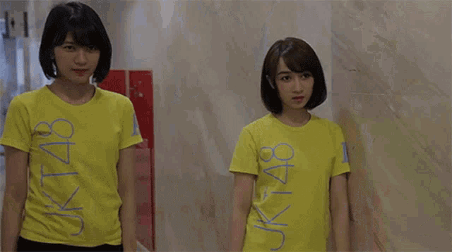 three women wearing yellow shirts with jk48 written on them