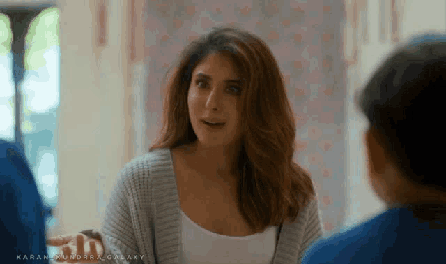 a woman in a gray cardigan is talking to a boy in a blue shirt .