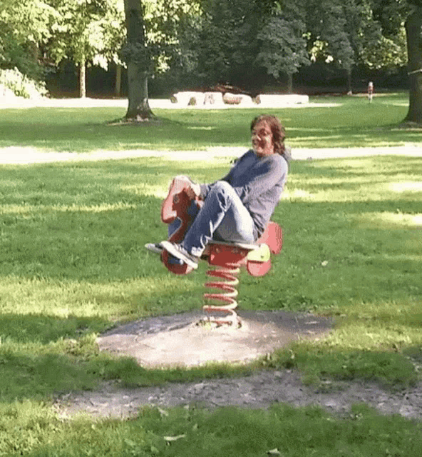 a woman is sitting on a rocking horse in a park .