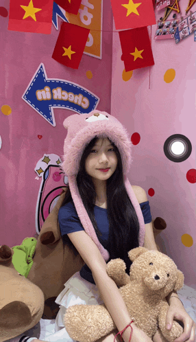 a girl in a pink hat holds a teddy bear in front of a sign that says check it out