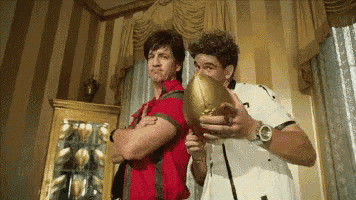 a man in a red shirt is holding a football next to another man in a white shirt