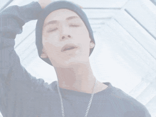 a man with his eyes closed wearing a blue beanie and a chain around his neck