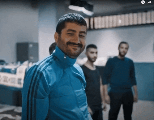 a man in a blue adidas jacket smiles in front of a group of men