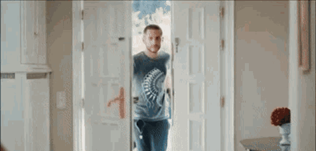 a man in a t-shirt is walking through a doorway in a living room .