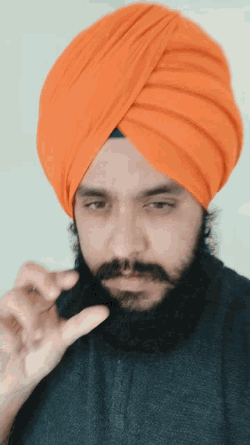 a man with a beard wearing an orange turban looks down