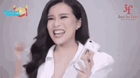 a woman in a white shirt is holding a cell phone in her hand and smiling .