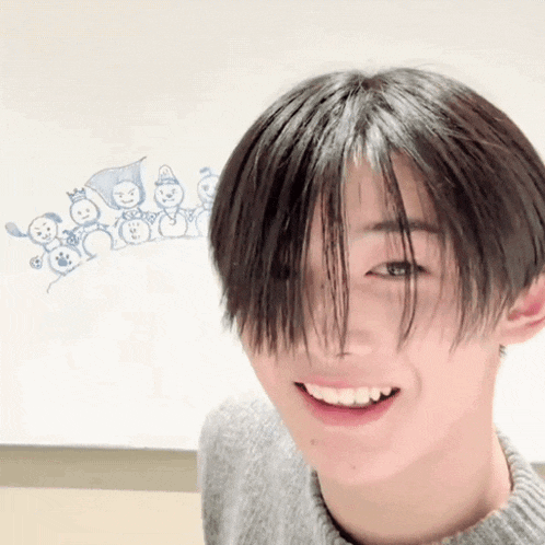 a young man with short hair is smiling in front of a white board with drawings on it .