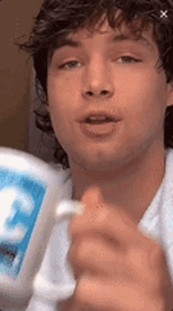 a young man with curly hair is holding a toothbrush and a bottle of toothpaste .