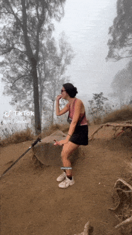 a woman sitting on a rock with a hiking pole in front of a foggy forest with tiktok written on the bottom