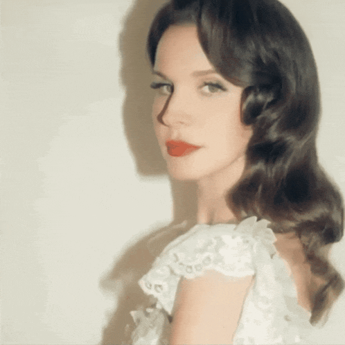 a woman in a white lace dress with red lipstick looks at the camera