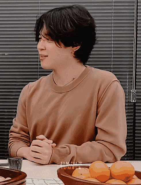 a young man sitting at a table with a bowl of oranges in front of him