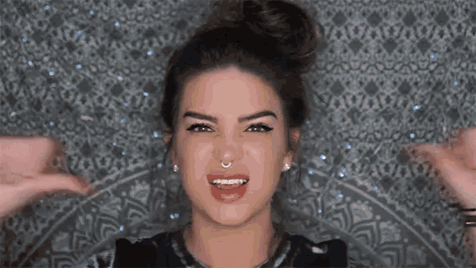 a woman with a nose ring is smiling and making a funny face with her hands .