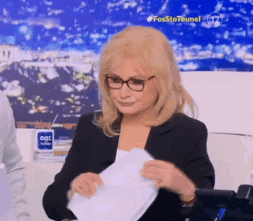 a woman wearing glasses is holding a piece of paper in her hand .