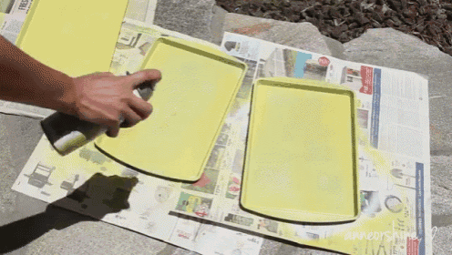 a person spraying yellow paint on a tray with a newspaper on the ground