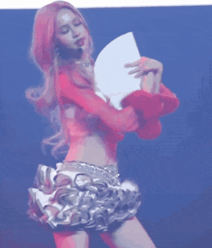 a woman in a pink top and skirt is holding a fan .