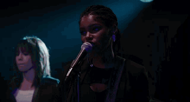 a woman is singing into a microphone in a dark room while another woman plays a guitar .