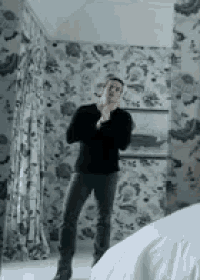 a man in a black sweater is standing in a room with floral wallpaper .