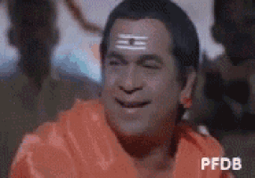 a man with a triangle on his forehead is smiling and wearing an orange robe .