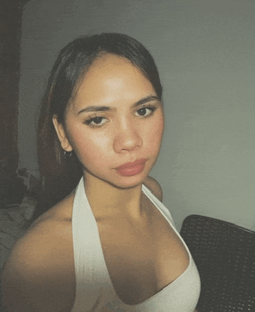 a young woman in a white tank top looks at the camera