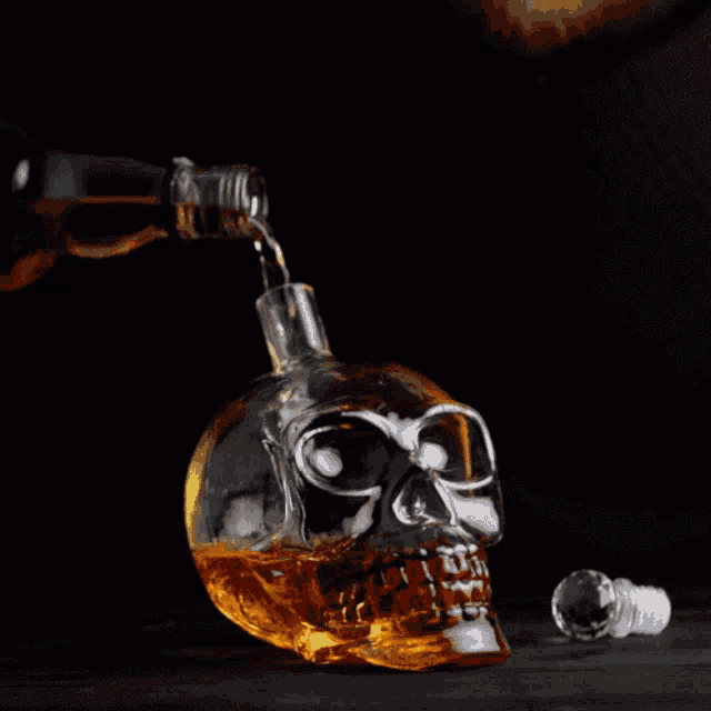 a bottle of alcohol is being poured into a glass skull shaped container