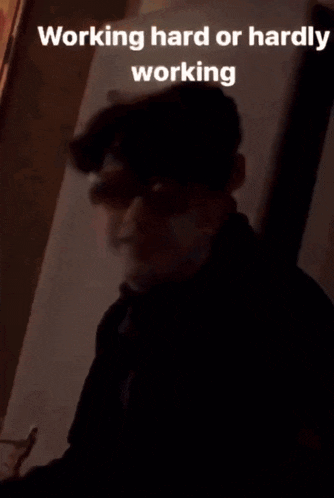 a young man wearing sunglasses and a black jacket is sitting in front of a wall .