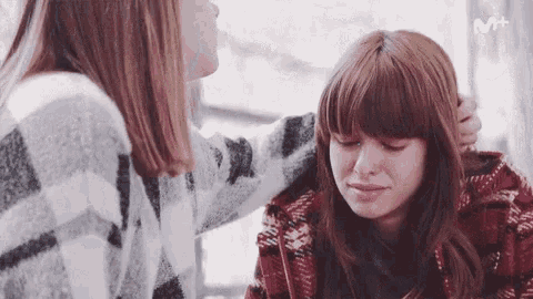 a woman is comforting another woman who is crying with a m + logo in the background