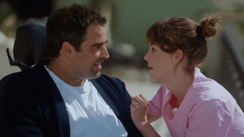 a man in a wheelchair and a woman in a pink scrub are looking at each other