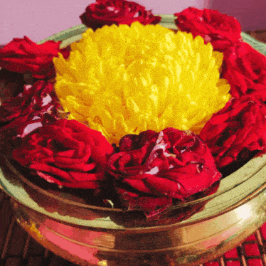 a bowl of red roses and yellow flowers on a table