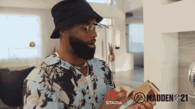 a man wearing a hat and glasses is holding a video game with madden 21 on the screen