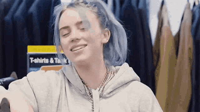 billie eilish is wearing a gray hoodie and smiling while standing in a store .