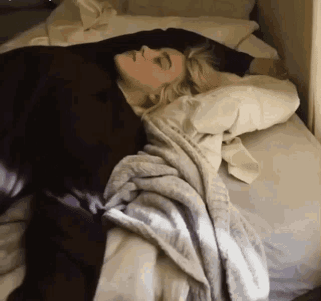 a woman is laying on a bed with a blanket on top of her