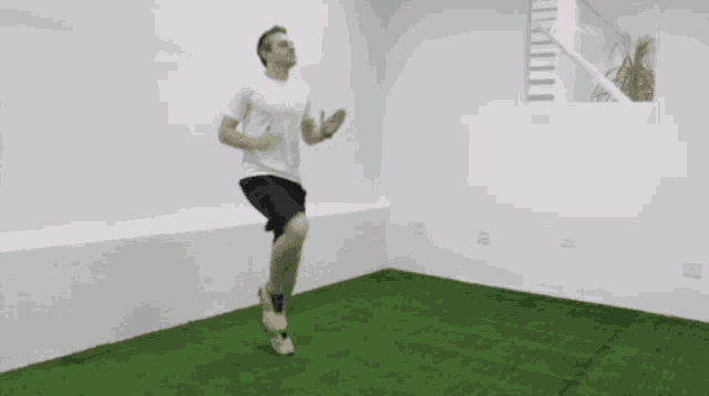 a man in a white shirt and black shorts is jumping on a green floor