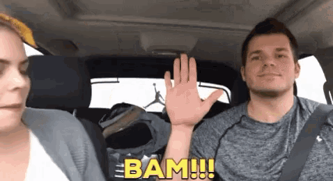 a man and a woman are in a car and the man is waving his hand and the woman is saying bam !!!