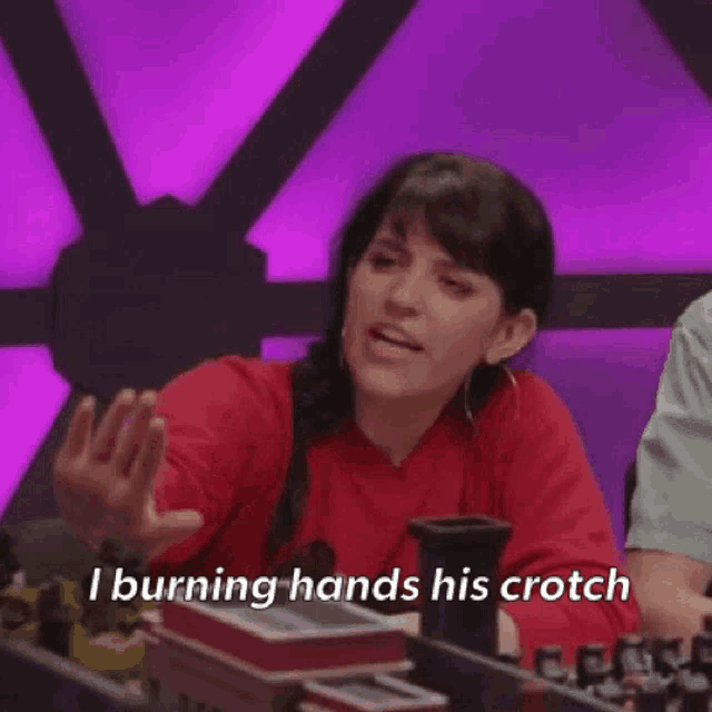 a woman in a red sweater is sitting at a table with a purple background and talking about burning hands his crotch .