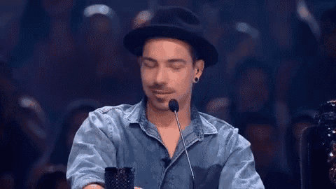 a man wearing a hat is sitting in front of a microphone .
