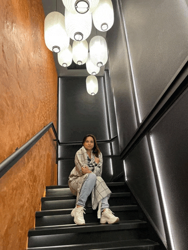 a woman is sitting on a set of stairs with lanterns hanging from the ceiling above her