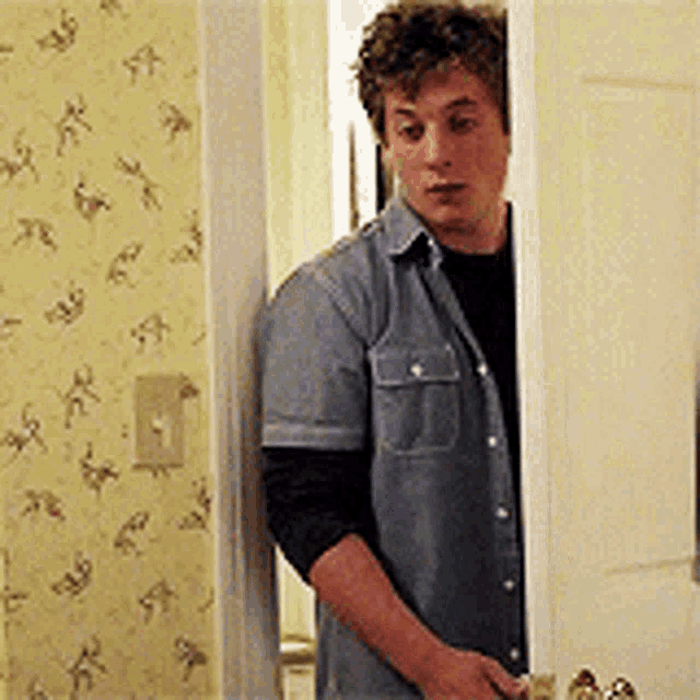 a man in a denim shirt is peeking out from behind a door